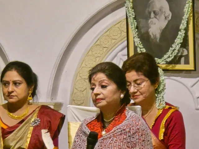 Three performers in saris seated beneath a garlanded portrait of Tagore
