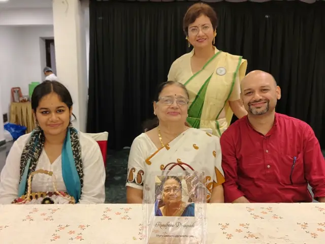 Three generations seated together with the host standing behind them